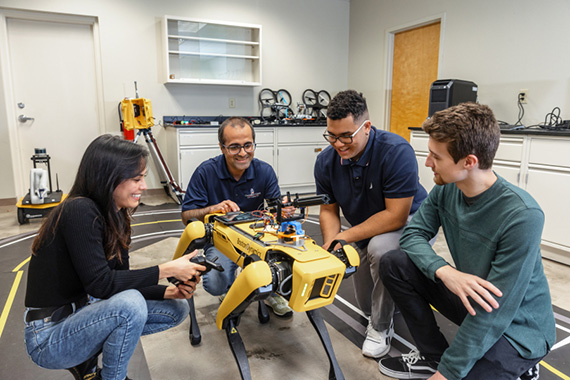 a professor discussing a yellow dog robot with three students