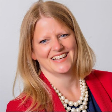 a woman wearing a black suit leaning against a wall with her arms crossed