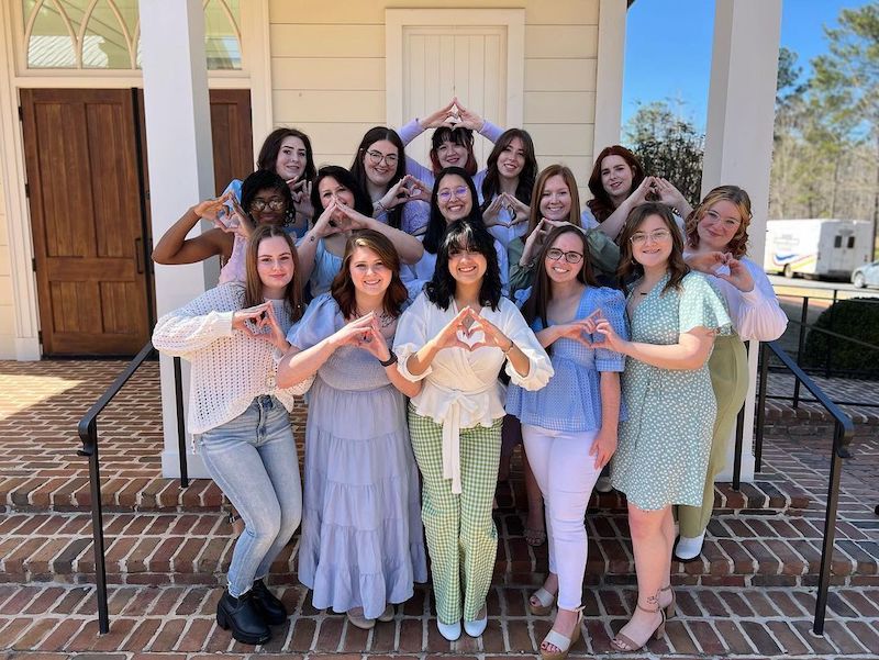 Sorority members posing outside, smiling, all making the same hand symbols