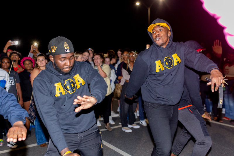 Two students dancing outside with others looking on